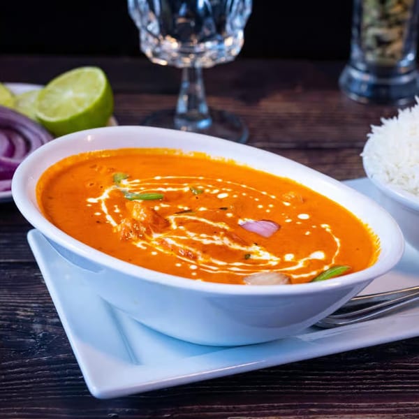 A bowl of Amaravati Indian Cuisine's orange curry with cream swirls, served with rice and lime.