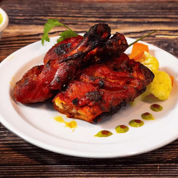 Amaravati Indian Cuisine's Tandoori Chicken, garnished with cilantro, vegetables, and sauces on a white plate.