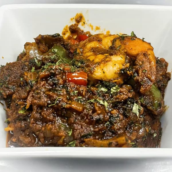 Indian shrimp curry with red and green peppers, garnished with fresh herbs in a white bowl.