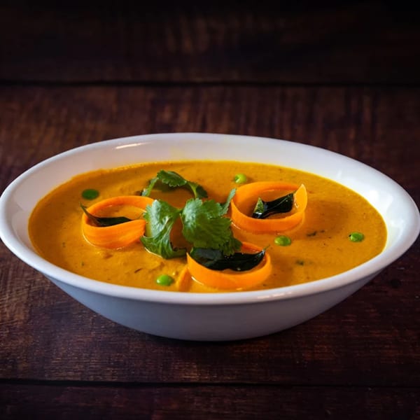 Amaravati Indian Cuisine's yellow curry with carrot ribbons, green peas, and cilantro in a white bowl.