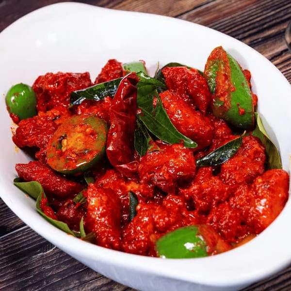 Amaravati Indian Cuisine's bright red chicken dish with green peppers and curry leaves in a white bowl.